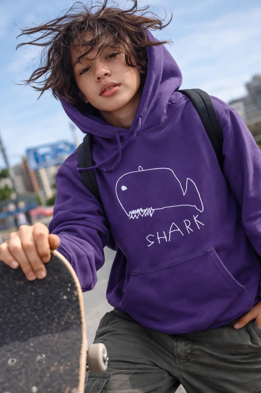 Person wearing a purple hoodie with a shark design, holding a skateboard outdoors.
