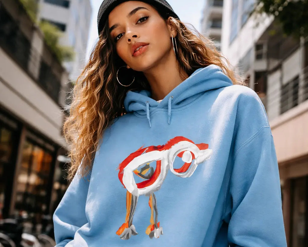 A young woman models the Mini Masterpiece Hoodie in a sunlit urban environment, showcasing a bold, playful design created from real child artwork. This lifestyle image emphasizes the hoodie’s soft fleece comfort, contemporary streetwear appeal, and its identity as a unique, artistic fashion piece.